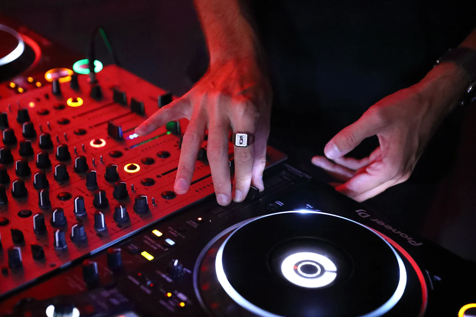 SOLONSKY's hands on a Pioneer DJ mixer under red light
